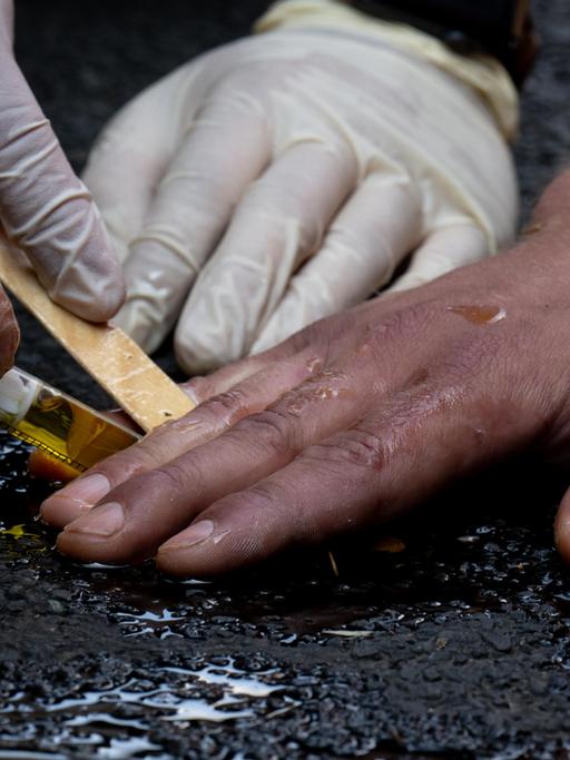 Polizeibeamte entfernen die festgeklebte Hand eines Klimaaktivisten der Gruppe "Letzte Generation" mit Olivenöl von einer Straße.