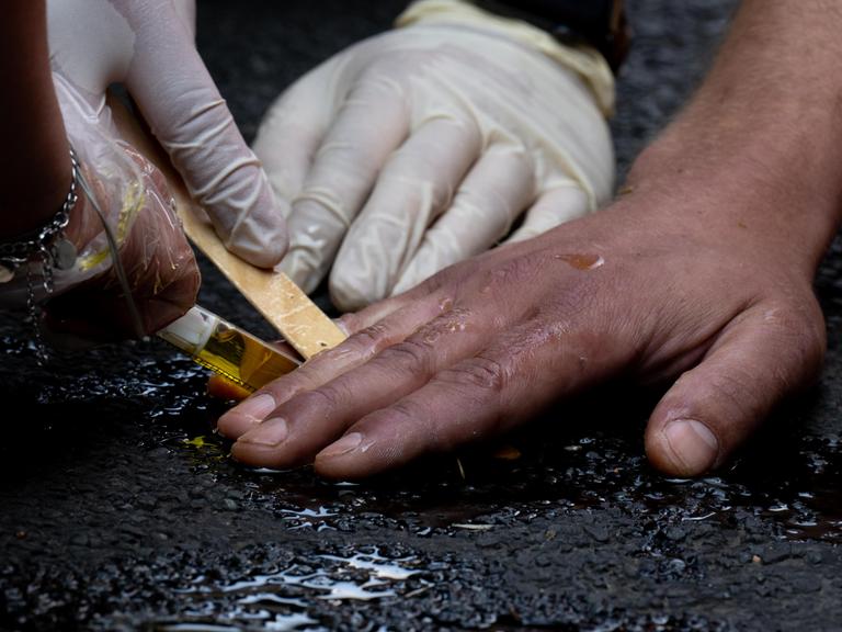Polizeibeamte entfernen die festgeklebte Hand eines Klimaaktivisten der Gruppe "Letzte Generation" mit Olivenöl von einer Straße.