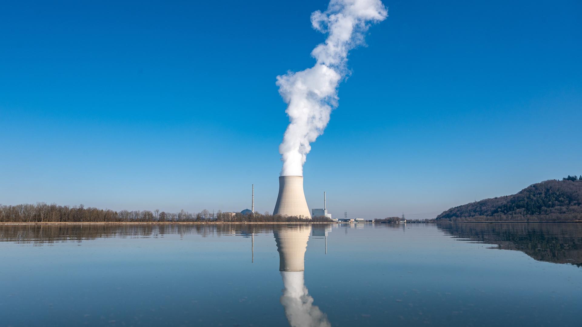 Aus dem Kühlturm eines Atomkraftwerks steigt weißer Dampf auf. Der Kühlturm spiegelt sich im Wasser. 