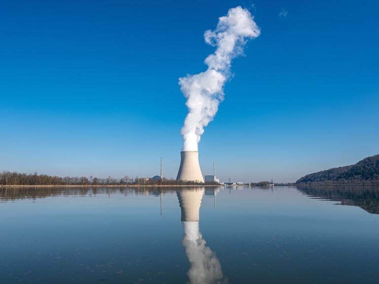Aus dem Kühlturm eines Atomkraftwerks steigt weißer Dampf auf. Der Kühlturm spiegelt sich im Wasser. 