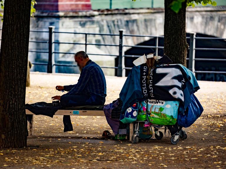 Ein Obdachloser sitzt auf einer Bank im Schatten der Bäume im Lustgarten auf der Museumsinsel in Berlin.
