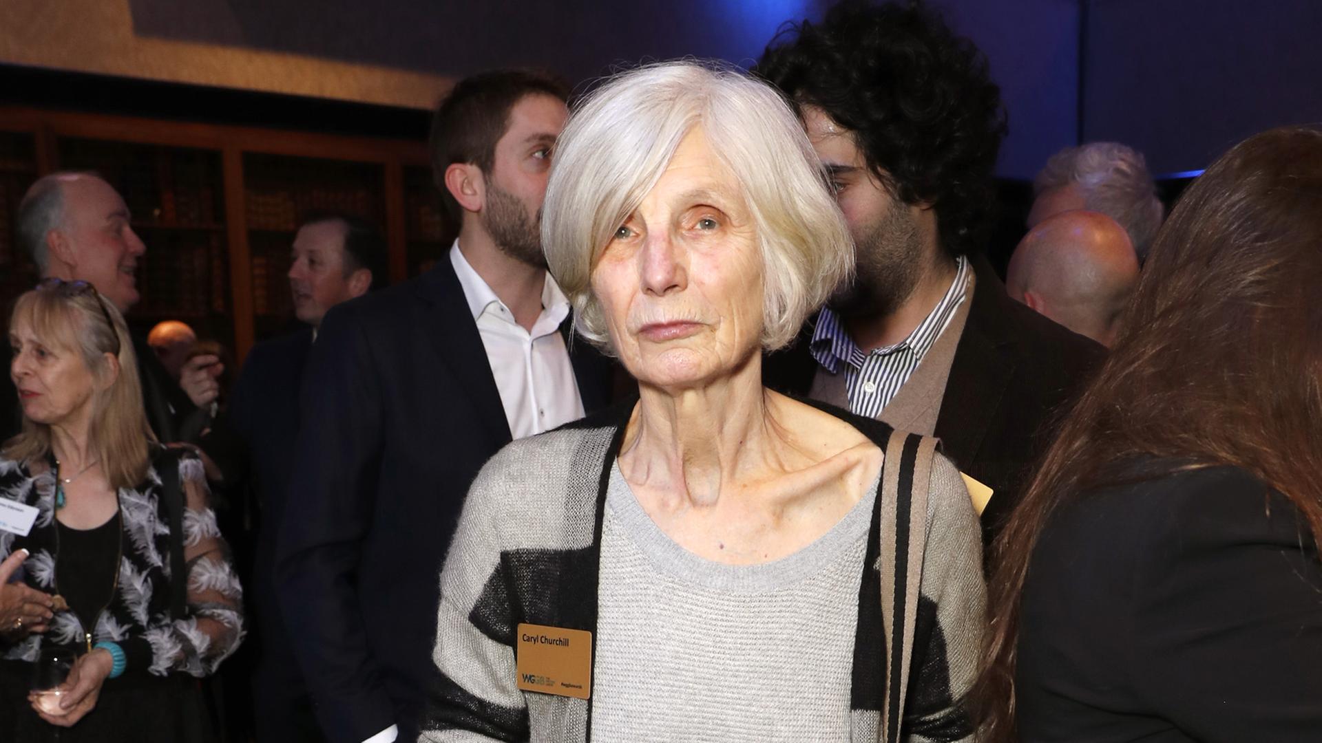 Die britische Autorin Caryl Churchill steht mit einem Getränk in der Hand vor anderen Personen Die britische Autorin Caryl Churchill steht mit einem Getränk in der Hand vor anderen Personen