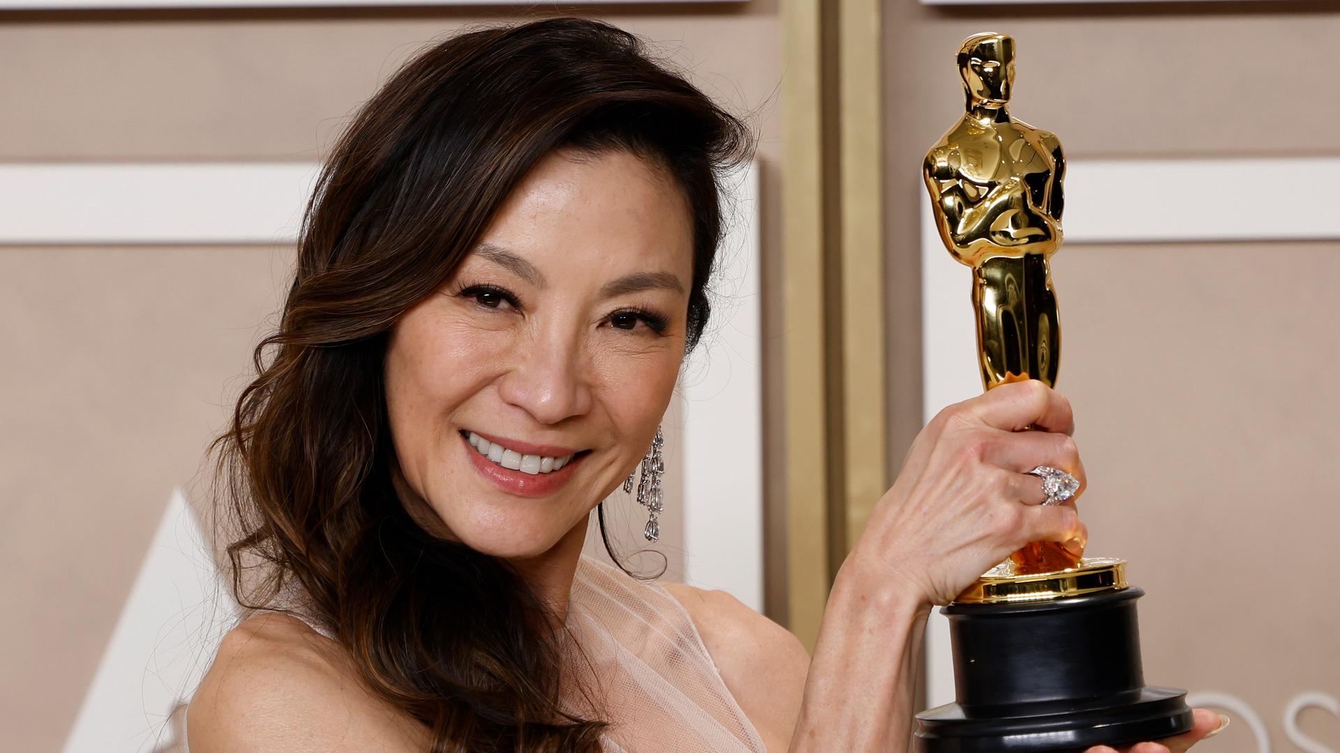 Die Schauspielerin Michelle Yeoh hält lächelnd ihre goldene Oscar-Statuette in die Kamera. Die Schauspielerin Michelle Yeoh hält lächelnd ihre goldene Oscar-Statuette in die Kamera.
