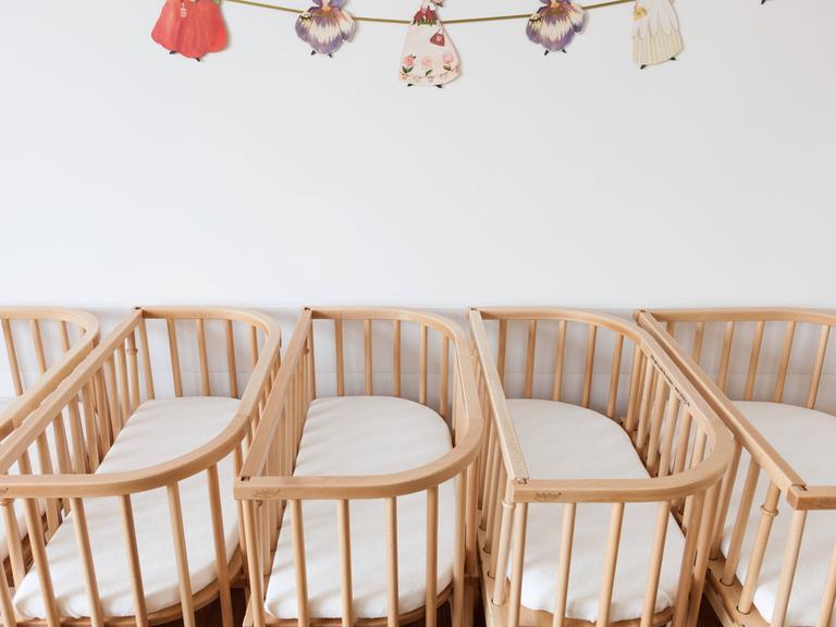 Leere Kinderbetten aus Holz stehen dicht nebeneinander.