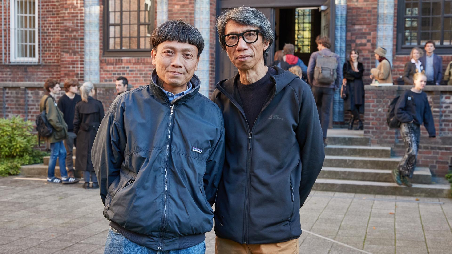 Die Ruangrupa-Mitglieder Reza Afisina (l) und Iswanto Hartono stehen vor dem Eingang der Hochschule für bildende Künste Hamburg