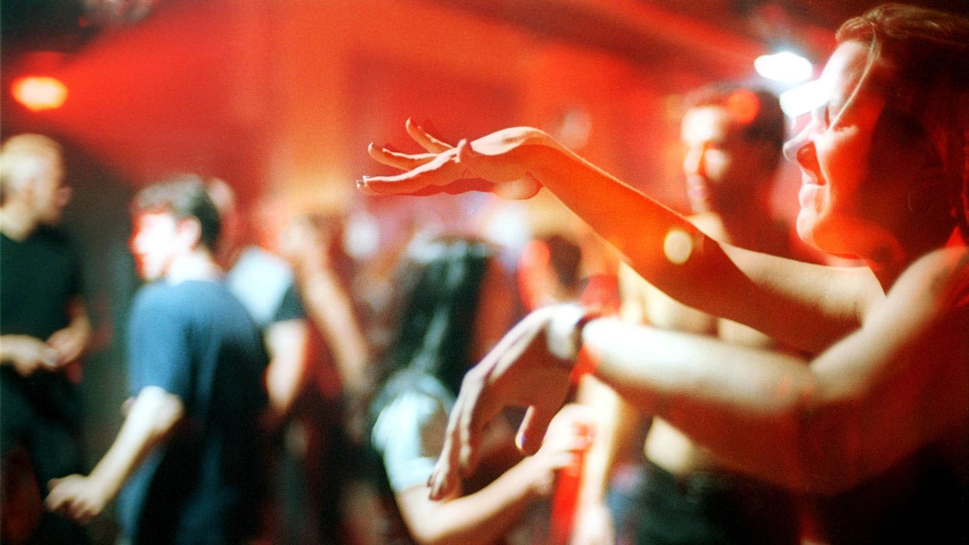 Ekstatisch tanzende Clubgänger im Berliner Club Tresor. Im Vordergrund rechts tanzt ein Mensch mit geschlossenen Augen und bewegt die Hände vor sich zur Musik.