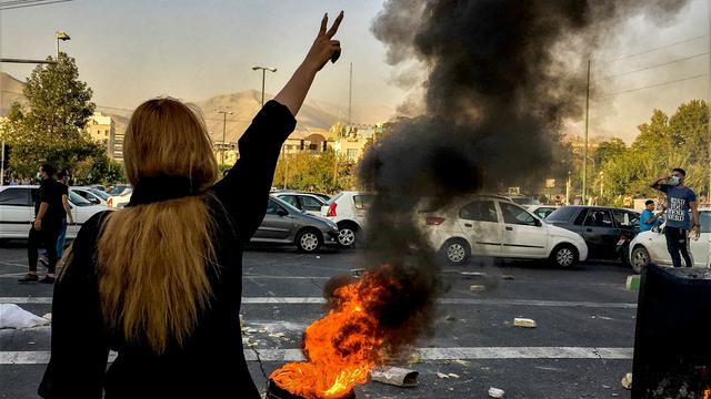 Eine Frau steht während einer Demonstration in Teheran vor einem brennenden Autoreifen und zeigt das Victory-Zeichen.