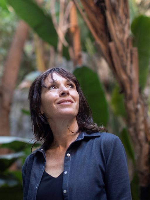 Rachel Cusk steht vor Palmen und blickt glücklich nach oben.