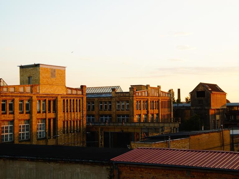 Ein großes, altes Fabrikgebäude  aus dunkelrotem Ziegelstein in der Abendsonne.