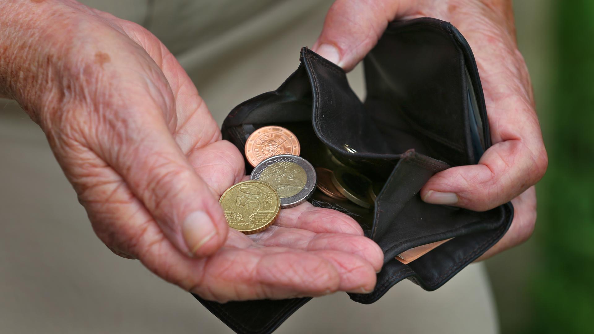 Eine Rentnerin hält einen Geldbeutel mit drei verschiedenen Euromünzen Eine Rentnerin hält einen Geldbeutel mit drei verschiedenen Euromünzen