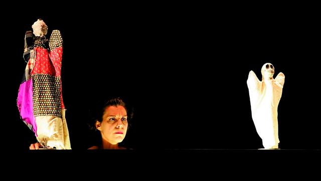 Der Kopf der Sängerin Salome Kammer ist im Scheinwerferlicht vor schwarzem Bühnenhintergrund zwischen zwei Puppen zu sehen 