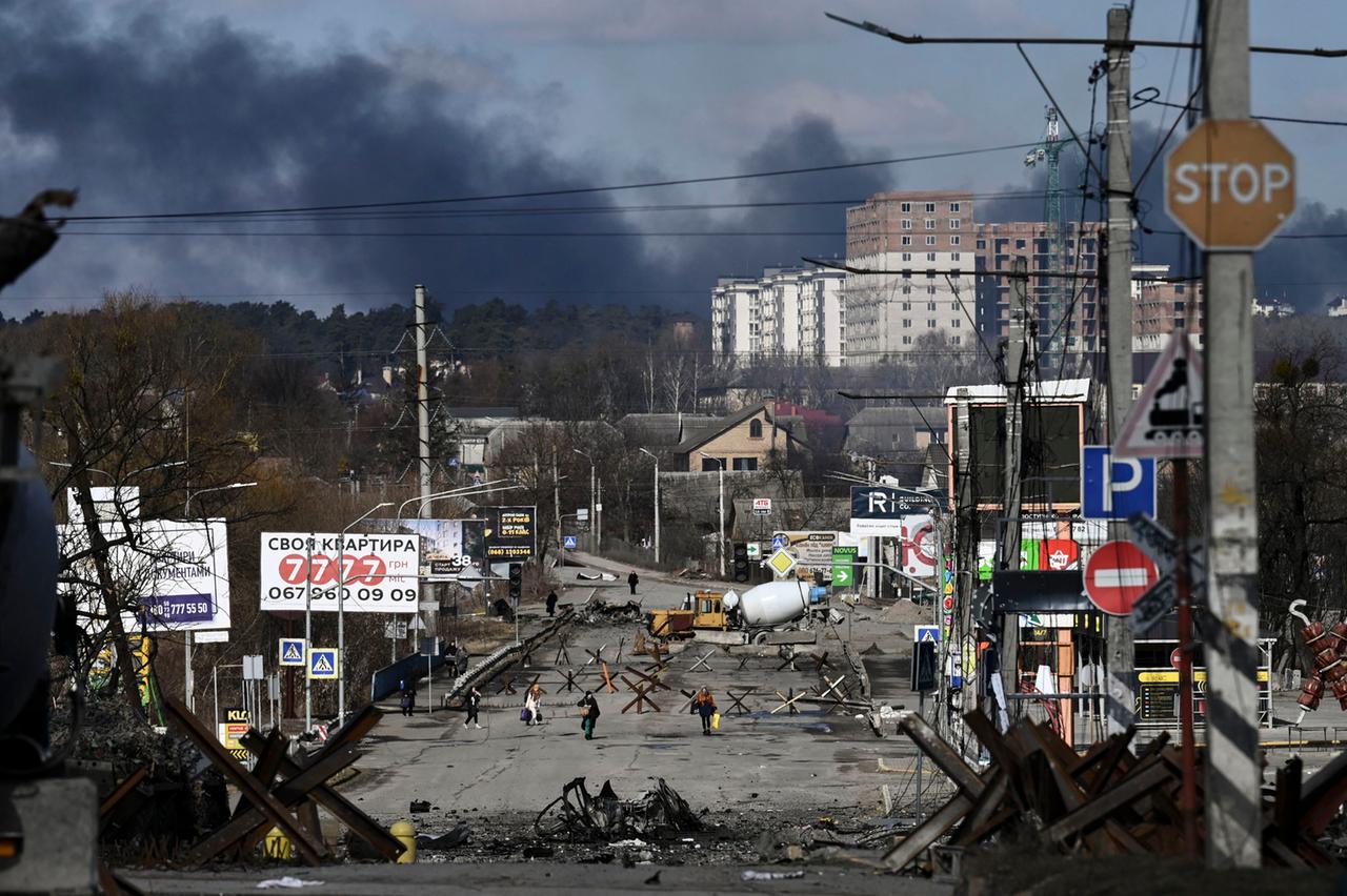 Menschen laufen nach einem Bombenangriff in der Nähe der Stadt Irpin bei Kiew in der Ukraine mit ihren Koffern über die Straße. Im Hintergrund eine schwarze Rauchwolke. Auf der Straße stehen Abwehrsperren. Menschen laufen nach einem Bombenangriff in der Nähe der Stadt Irpin bei Kiew in der Ukraine mit ihren Koffern über die Straße. Im Hintergrund eine schwarze Rauchwolke. Auf der Straße stehen Abwehrsperren.