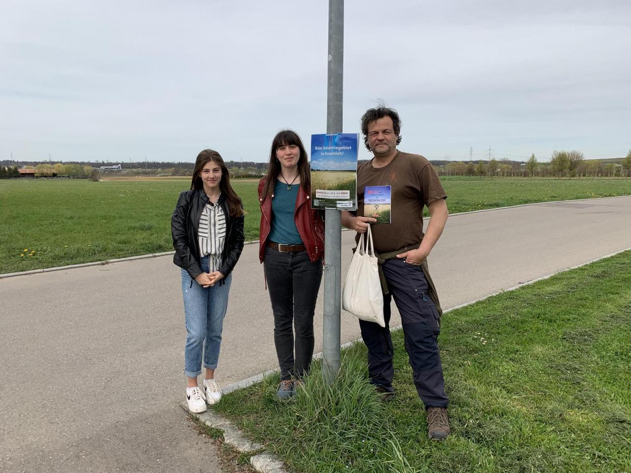 Zwei Frauen und ein Mann stehen an einem Verkehrsschild vor einer Wiese Zwei Frauen und ein Mann stehen an einem Verkehrsschild vor einer Wiese