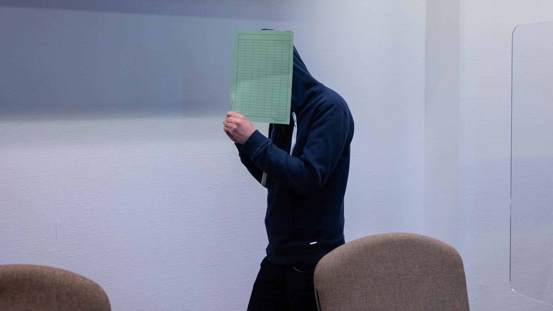 Der Mann aus Wermelskirchen im Gerichts-Saal. Er hält sich eine grüne Mappe vor das Gesicht. Der Mann aus Wermelskirchen im Gerichts-Saal. Er hält sich eine grüne Mappe vor das Gesicht.