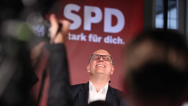 Der SPD-Spitzenkandidat und amtierende Bürgermeister Andreas Bovenschulte steht vor einem SPD-Logo und lacht.
