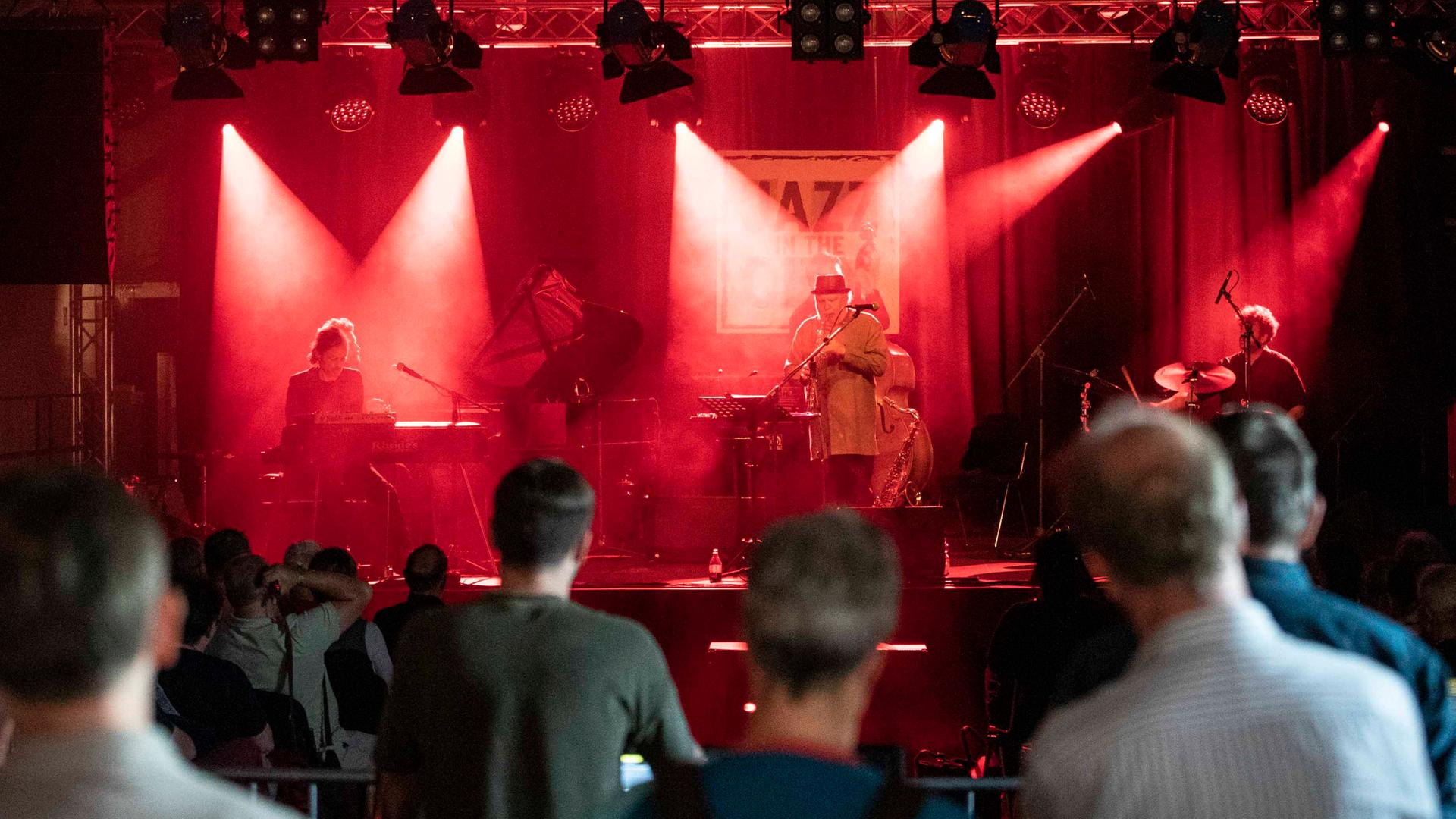 Konzert von Max Herre & Roberto di Gioia live auf dem Jazz in the City Festivals im Zughafen Erfurt. Man sieht die Zuschauer, die auf die Bühne blicken. Auf der Bühne stehen in rotes Licht getaucht die Musiker. Konzert von Max Herre & Roberto di Gioia live auf dem Jazz in the City Festivals im Zughafen Erfurt. Man sieht die Zuschauer, die auf die Bühne blicken. Auf der Bühne stehen in rotes Licht getaucht die Musiker.