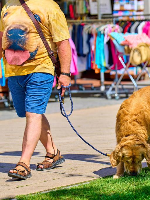 Ein Mann mit dem Bild seines Hundes auf dem T-Shirt geht mit seinem Hund spazieren.