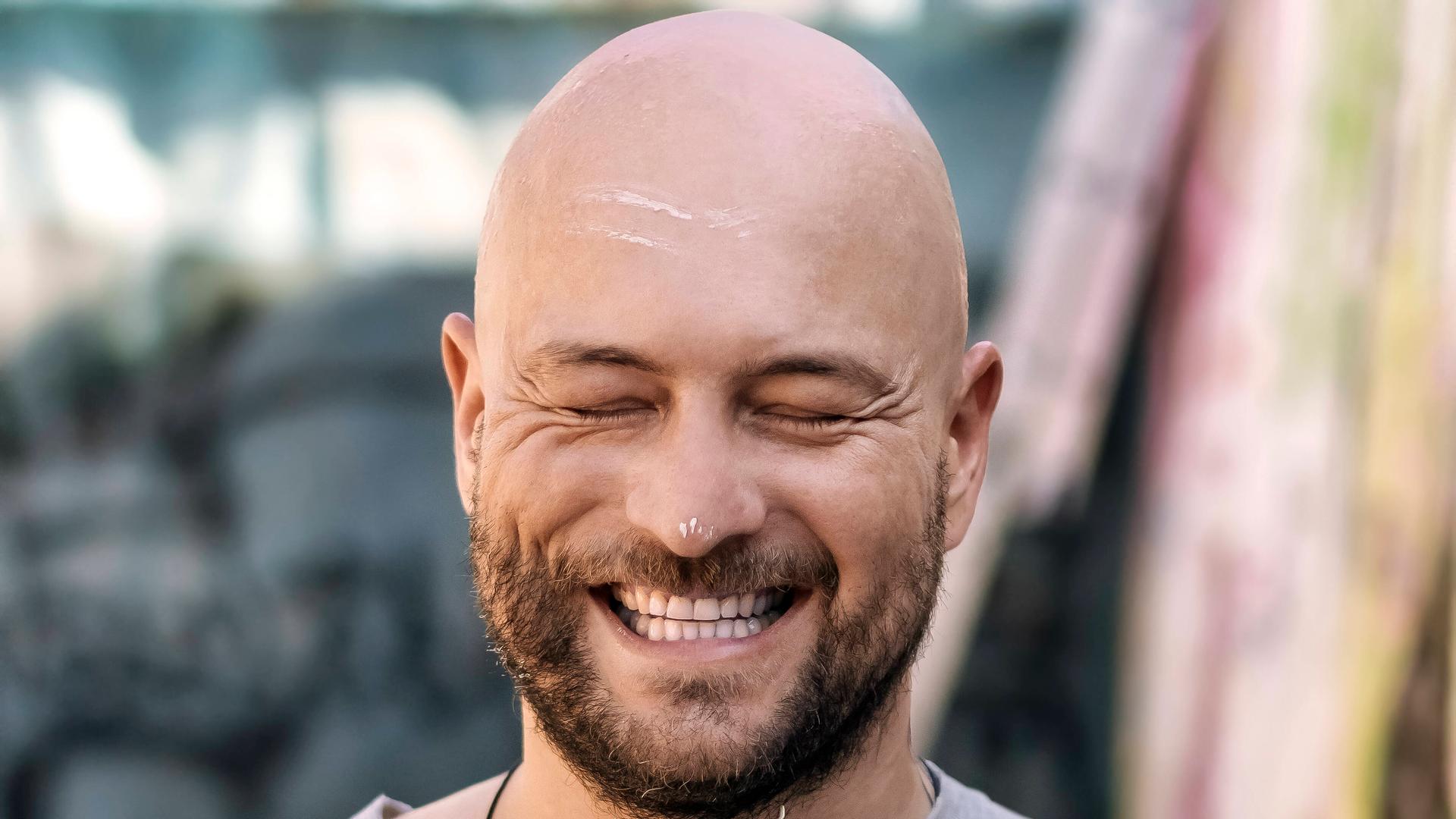 Ein lächelnder Mann mit Glatze, weißen Farbklecksen im Gesicht und einem Malerpinsel in der Hand. Ein lächelnder Mann mit Glatze, weißen Farbklecksen im Gesicht und einem Malerpinsel in der Hand.