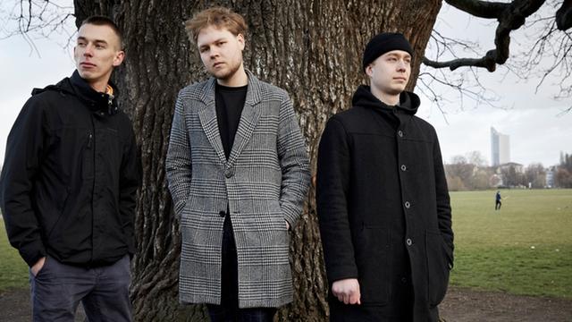 Drei Männer stehen vor einem Baum und schauen ernst in die Kamera. Es ist das Vincent Meissner Trio. 