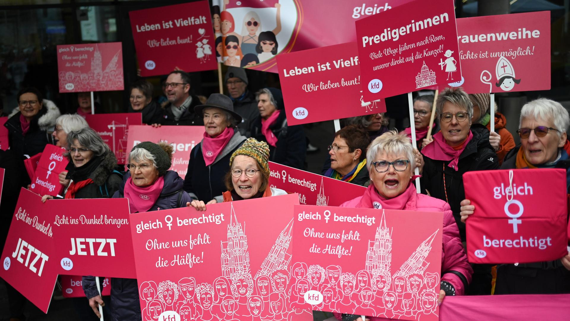Eine Gruppe von Frauen hält rosa Schilder hoch. Auf denen stehen Sachen wie "Ohne uns fehlt die Hälfte" oder "Gleichberechtigung".