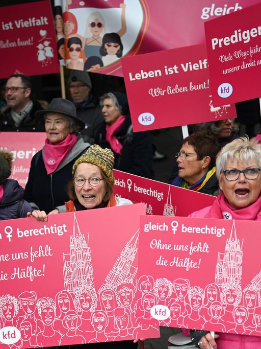 Eine Gruppe von Frauen hält rosa Schilder hoch. Auf denen stehen Sachen wie "Ohne uns fehlt die Hälfte" oder "Gleichberechtigung".