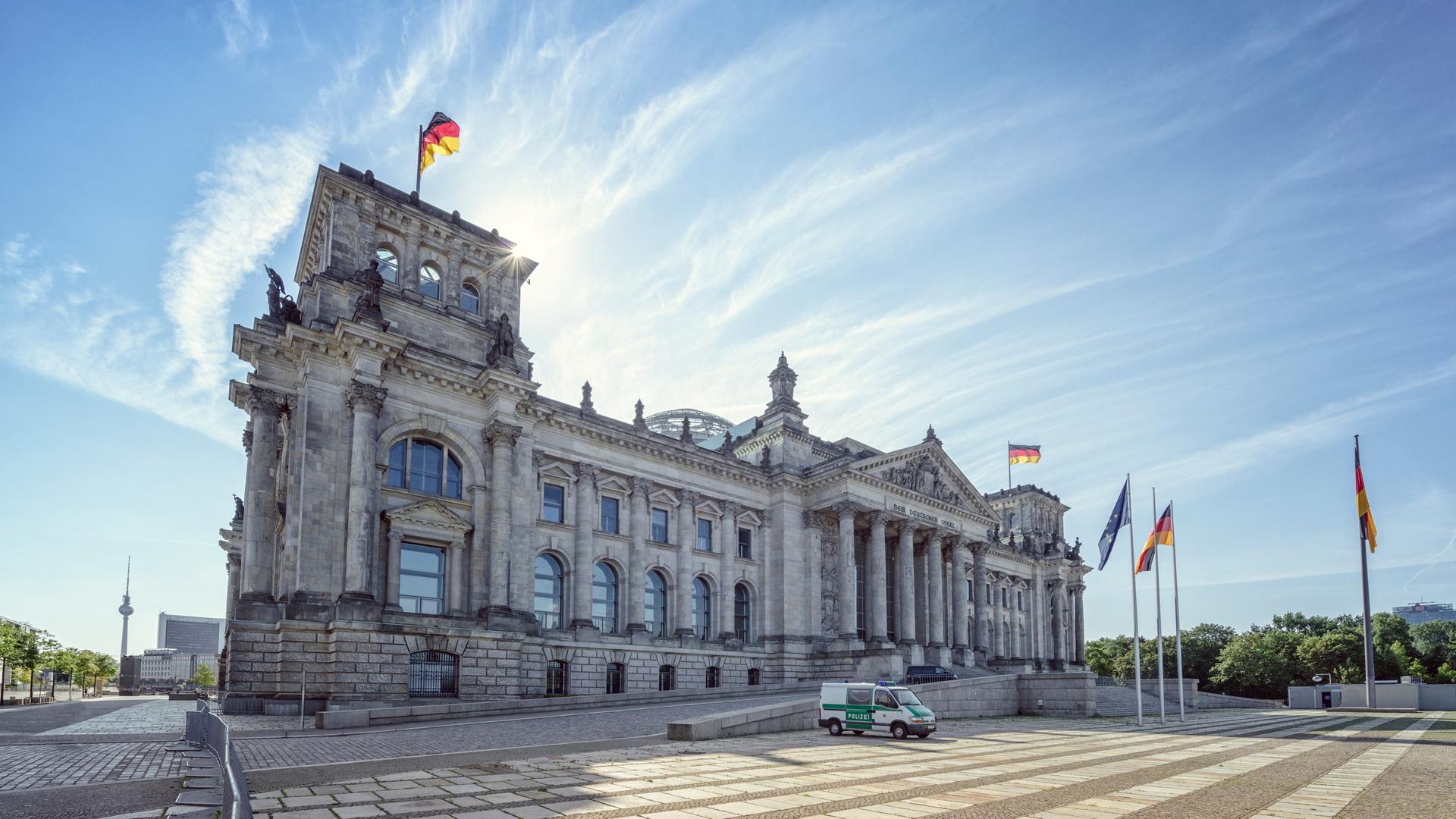 Das Reichstagsgebäude in Berlin, schräg von der Seite fotografiert. Davor ein Polizeifahrzeug. Im Hintergrund blauer Himmel.