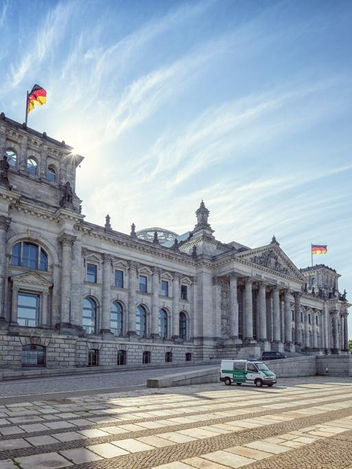 Das Reichstagsgebäude in Berlin, schräg von der Seite fotografiert. Davor ein Polizeifahrzeug. Im Hintergrund blauer Himmel.