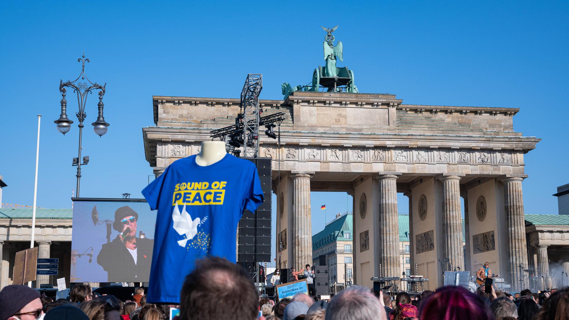 Zuschauer vor dem Brandenburger Tor verfolgen das Geschehen bei der Friedensaktion "Sound of Peace", während Marius Müller-Westernhagen auf einem Bildschirm zu sehen ist.