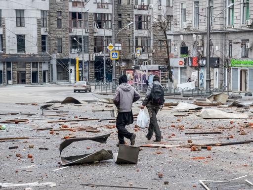 Zwei Männer laufen in Charkiw über Trümmerteile auf der Straße nach dem Beschuss durch russische Truppen.