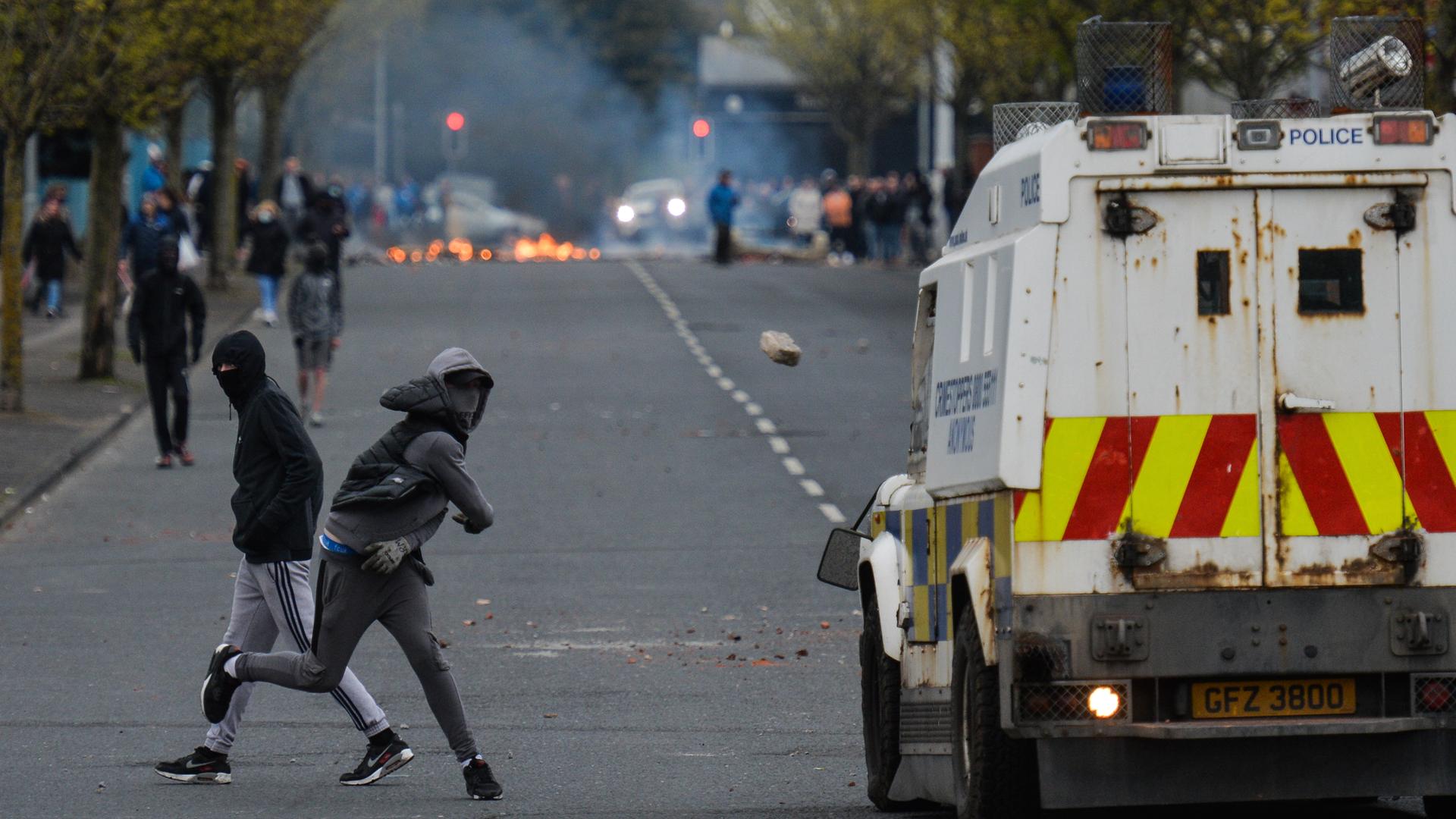Ein vermummter junger Mann wirft einen Stein auf ein Polizeiauto bei Protesten im April 2021 in Belfast.