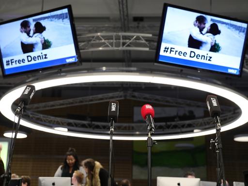 16.02.2018, Berlin:Â Mikrofone stehen vor der Pressekonferenz anlässlich Freilassung des Â«WeltÂ»-Korrespondenten Deniz Yücel im Newsroom der Zeitung "Die Welt" vor Bildschirmen, die ein Foto nach seiner Freilassung zeigen. Nach mehr als einem Jahr in türkischer Haft hat der Â«WeltÂ»-Korrespondent Deniz Yücel das Gefängnis in Silivri bei Istanbul verlassen. (zuÂ "Nach mehr als einem Jahr in türkischer Haft hat der Â«WeltÂ»-Korrespondent Deniz Yücel das Gefängnis in Silivri bei Istanbul verlassen"Â vom 16.02.2018) Foto: Kay Nietfeld/dpa +++ dpa-Bildfunk +++
