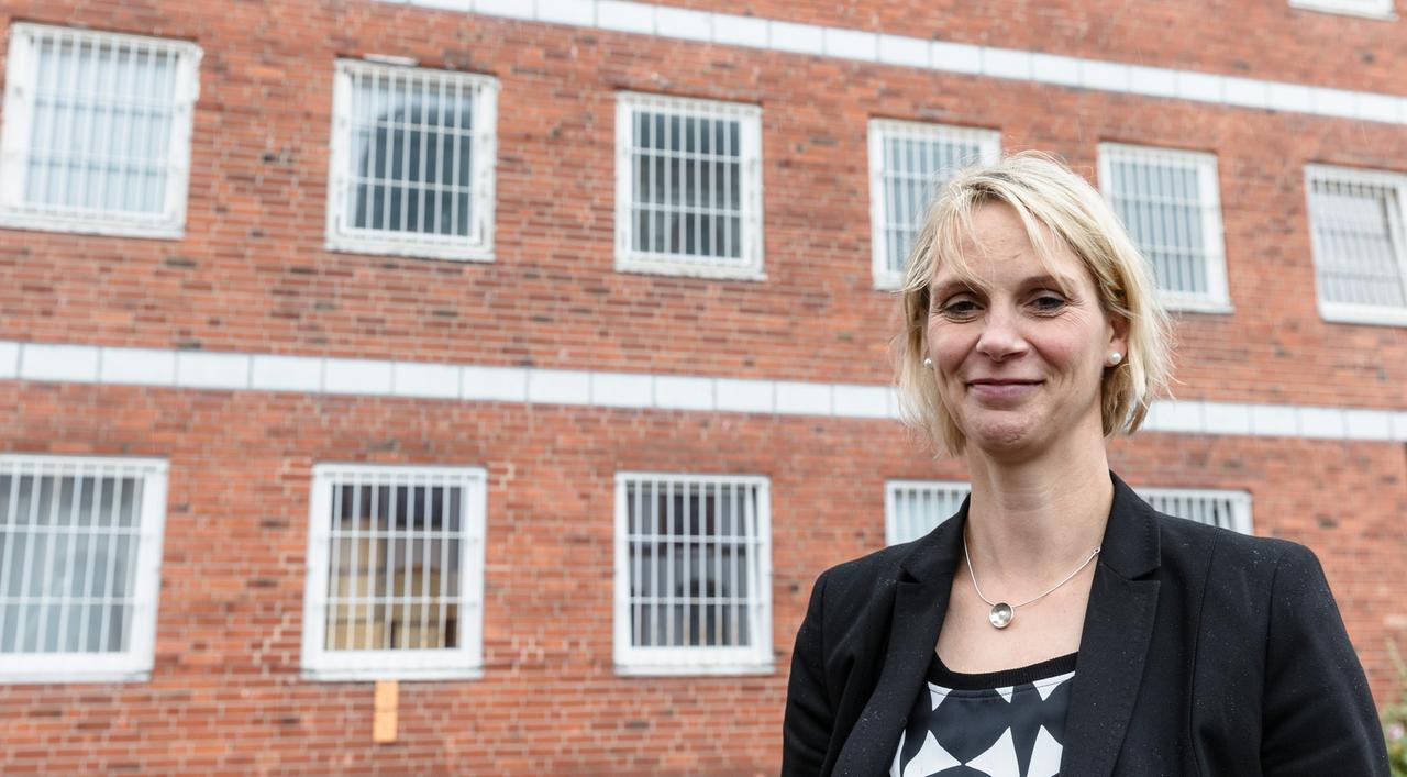 Eine blonde Frau in schwarzem Blazer steht vor eine Kachelsteinwand: Leiterin der Justizvollzugsanstalt Neumünster, Yvonne Radetzki. Eine blonde Frau in schwarzem Blazer steht vor eine Kachelsteinwand: Leiterin der Justizvollzugsanstalt Neumünster, Yvonne Radetzki.