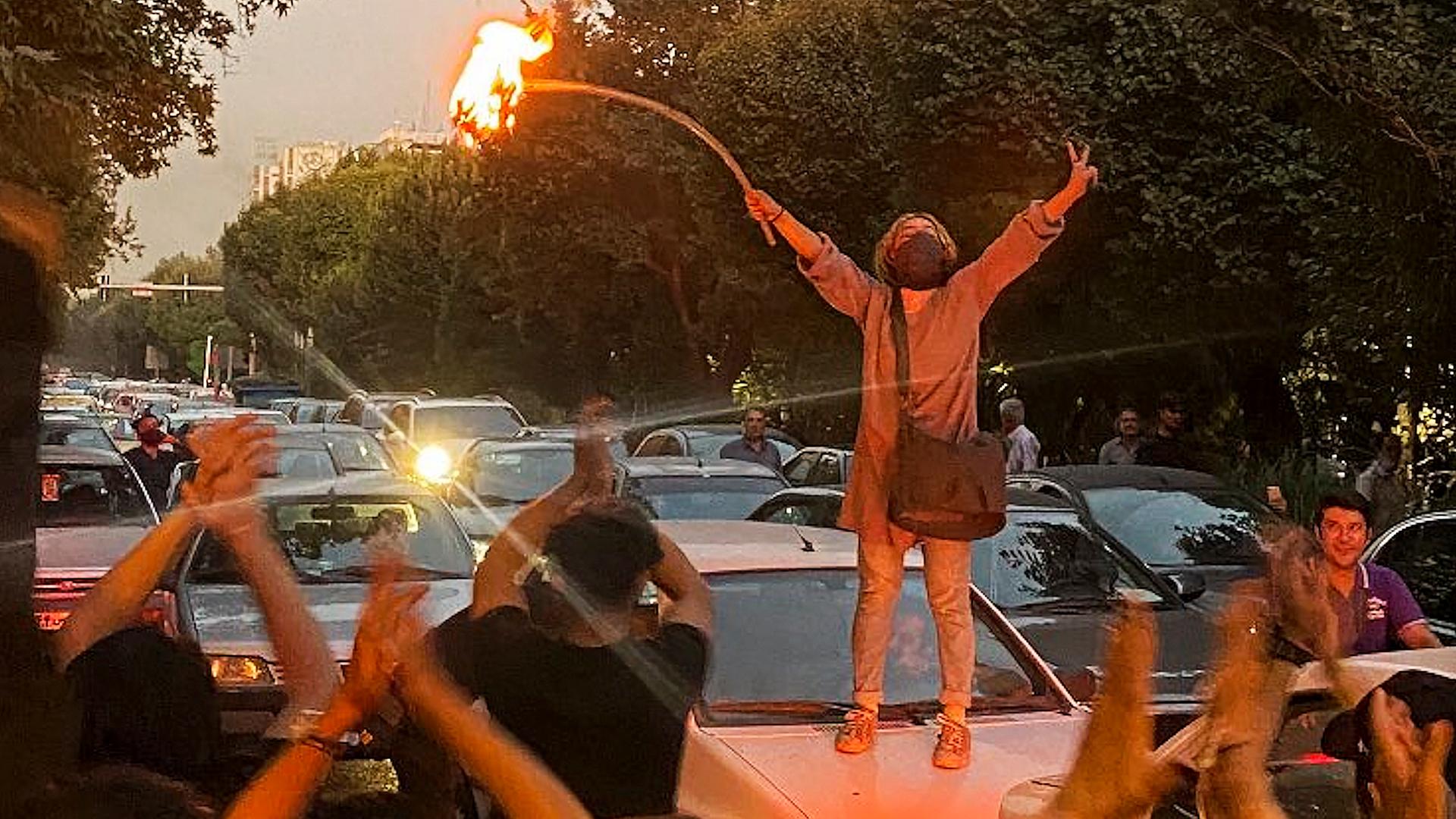 Eine Frau steht auf einem Auto bei Protesten in Teheran. Sie hat ihr Kopftuch abgelegt und die Arme zur Seite ausgestreckt. Eine Frau steht auf einem Auto bei Protesten in Teheran. Sie hat ihr Kopftuch abgelegt und die Arme zur Seite ausgestreckt.