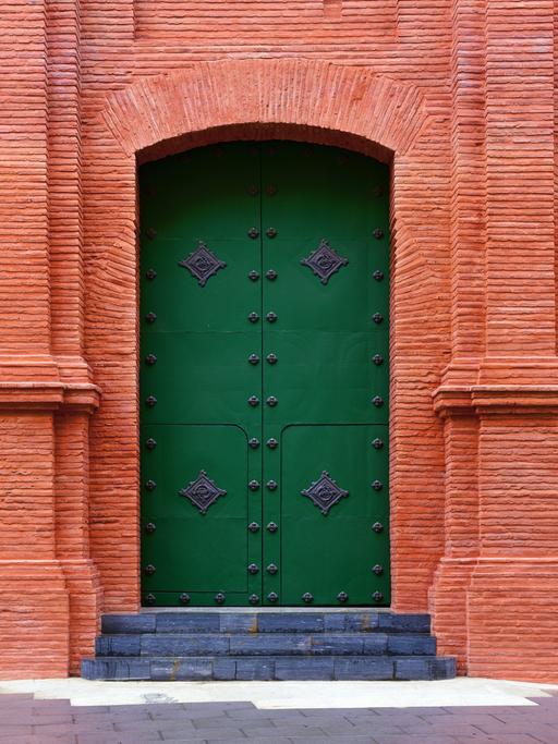 Außenansicht der Kathedrale von Cartagena mit rotem Tor, grüner Tür uns zwei Heiligenfiguren (Symbolbild)