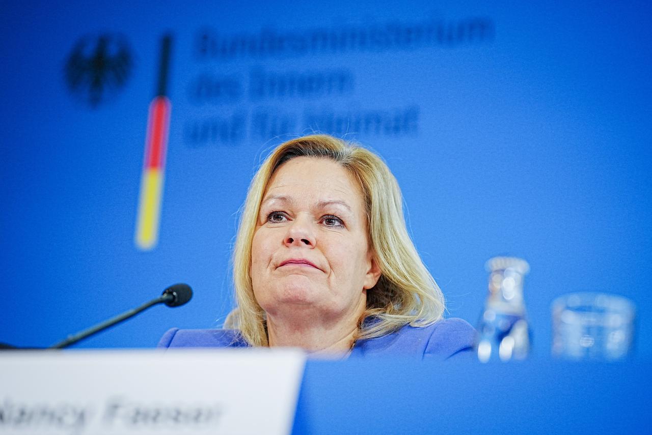 Bundesinnenministerin Faeser sitzt vor einem Mikrofon. Sie trägt einen blauen Blazer. Im Hintergrund sieht man den Schriftzug der Bundesregierung. 