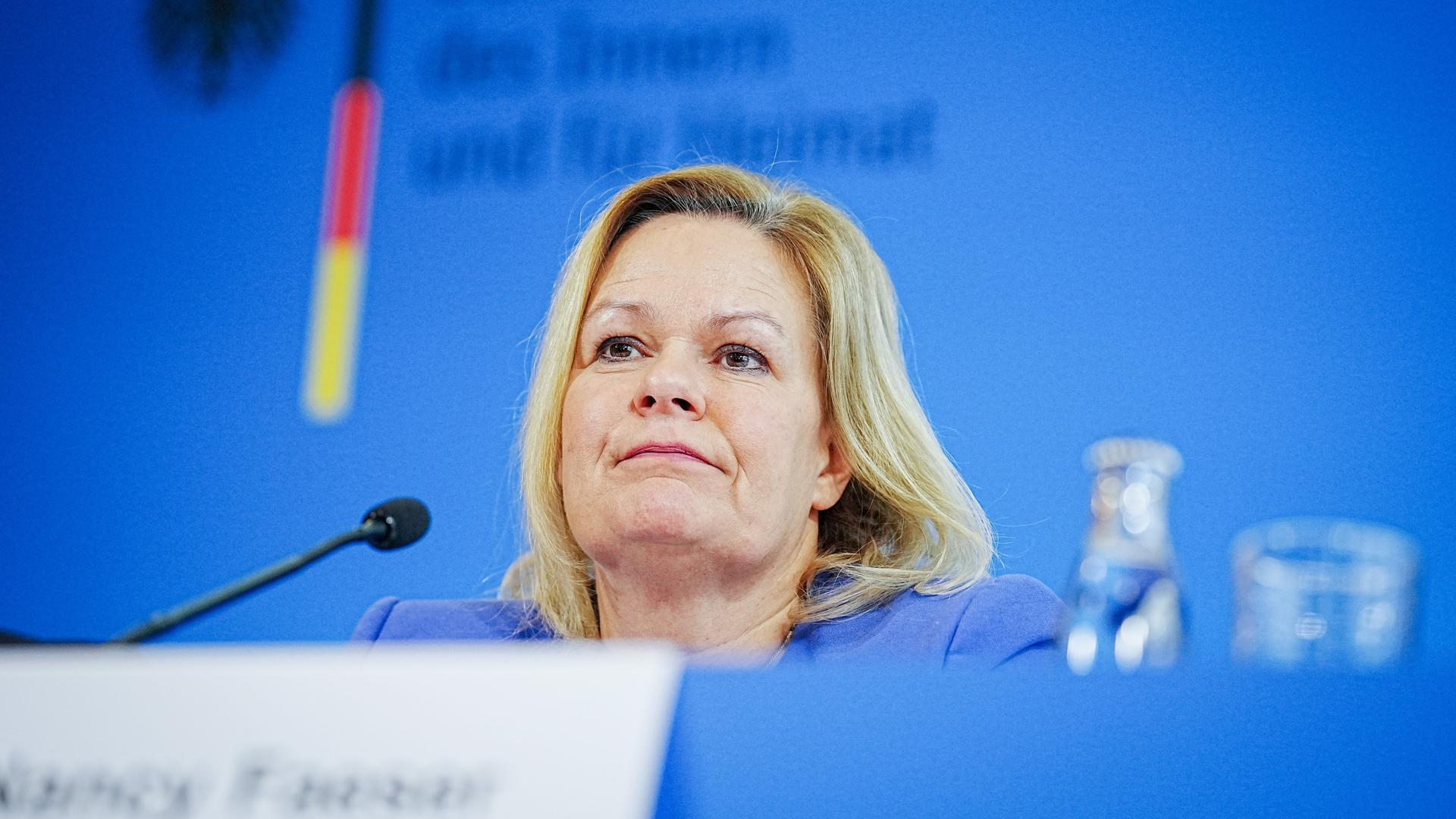 Bundesinnenministerin Faeser sitzt vor einem Mikrofon. Sie trägt einen blauen Blazer. Im Hintergrund sieht man den Schriftzug der Bundesregierung. Bundesinnenministerin Faeser sitzt vor einem Mikrofon. Sie trägt einen blauen Blazer. Im Hintergrund sieht man den Schriftzug der Bundesregierung.