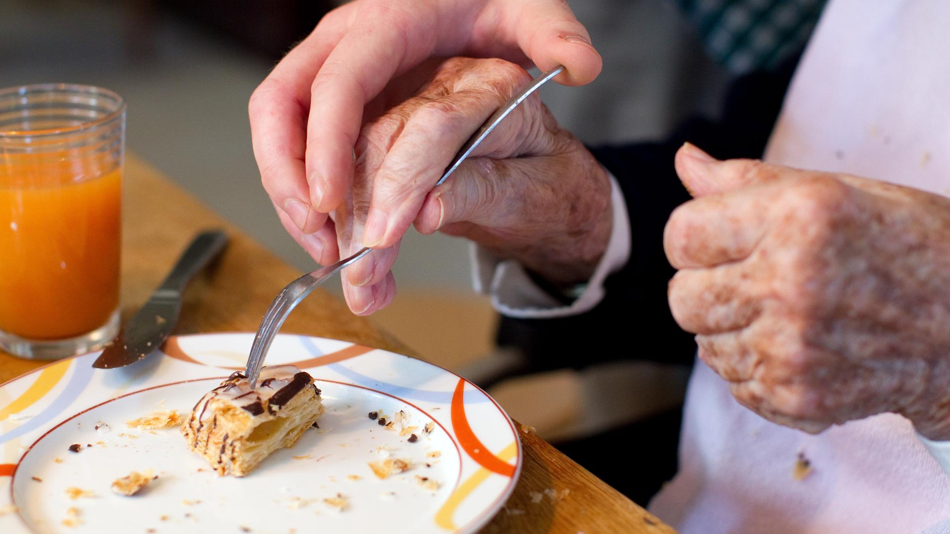 Ein junger Mann hilft einer Bewohnerin einer Alzheimer-Wohngemeinschaft beim Einnehmen einer Mahlzeit. Ein junger Mann hilft einer Bewohnerin einer Alzheimer-Wohngemeinschaft beim Einnehmen einer Mahlzeit.