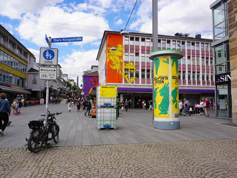 In Kassel hängt ein Documenta-Plakat an einer Litfaßsäule und ein Documenta-Banner an einem Haus.