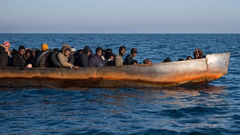 Geflüchtete Personen sitzen dicht gedrängt in einem Boot vor der italienischen Küste.
