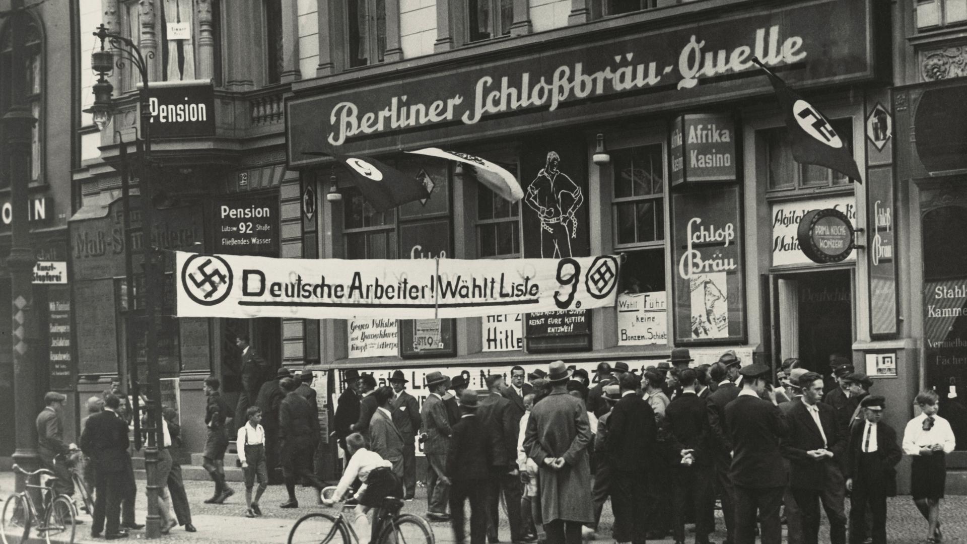 Historische Aufnahme vor einem Restaurant an dem "Berliner Schlossbräuquelle" steht. Davor ein Banner was zur Wahl der NSDAP auffordert. Historische Aufnahme vor einem Restaurant an dem "Berliner Schlossbräuquelle" steht. Davor ein Banner was zur Wahl der NSDAP auffordert.
