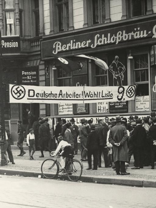 Historische Aufnahme vor einem Restaurant an dem "Berliner Schlossbräuquelle" steht. Davor ein Banner was zur Wahl der NSDAP auffordert.