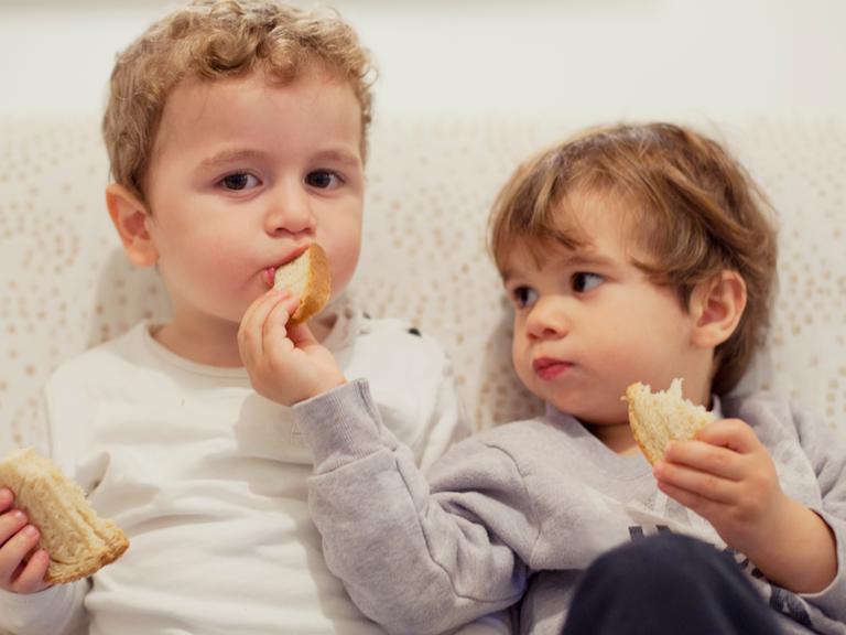 Zwei kleine Kinder teilen Brot.