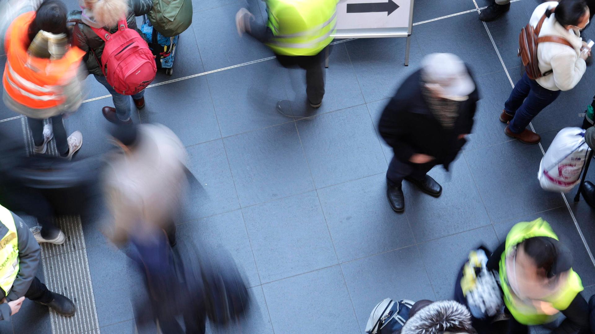 Eine Szene am Berliner Hauptbahnhof aus der Vogelperspektive: Ankunft geflüchteter Menschen aus der Ukraine am 12.3.22. Es gibt ein Hinweisschild mit der ukrainischen Flagge und einem Pfeil. Viele Menschen, manche mit Koffern, einige mit Warnwesten. Eine Szene am Berliner Hauptbahnhof aus der Vogelperspektive: Ankunft geflüchteter Menschen aus der Ukraine am 12.3.22. Es gibt ein Hinweisschild mit der ukrainischen Flagge und einem Pfeil. Viele Menschen, manche mit Koffern, einige mit Warnwesten.