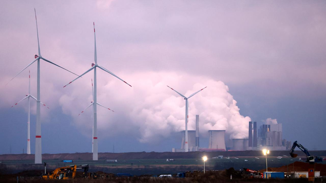 Windkraftanlagen stehen auf einem Feld, dahinter ein Kohlekraftwerk.