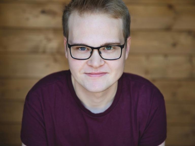 Ein junger Mann mit schwarzer Brille und dunklem T-Shirt