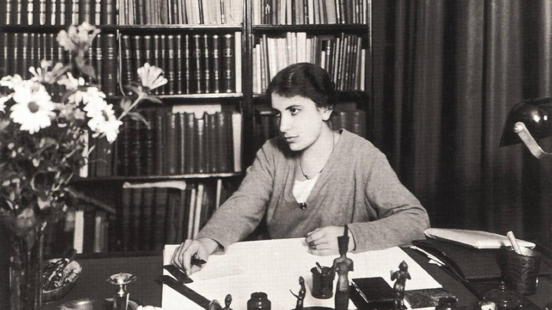 Das Foto zeigt Anna Freud, die jüngste Tochter von Sigmund Freud, in den 1920er-Jahren als junge Frau mit Kurzhaarschnitt. Sie sitzt hinter einem großen Schreibtisch vor einem Bücherregal und blickt nachdenklich schräg am Fotografen vorbei. Das Foto zeigt Anna Freud, die jüngste Tochter von Sigmund Freud, in den 1920er-Jahren als junge Frau mit Kurzhaarschnitt. Sie sitzt hinter einem großen Schreibtisch vor einem Bücherregal und blickt nachdenklich schräg am Fotografen vorbei.