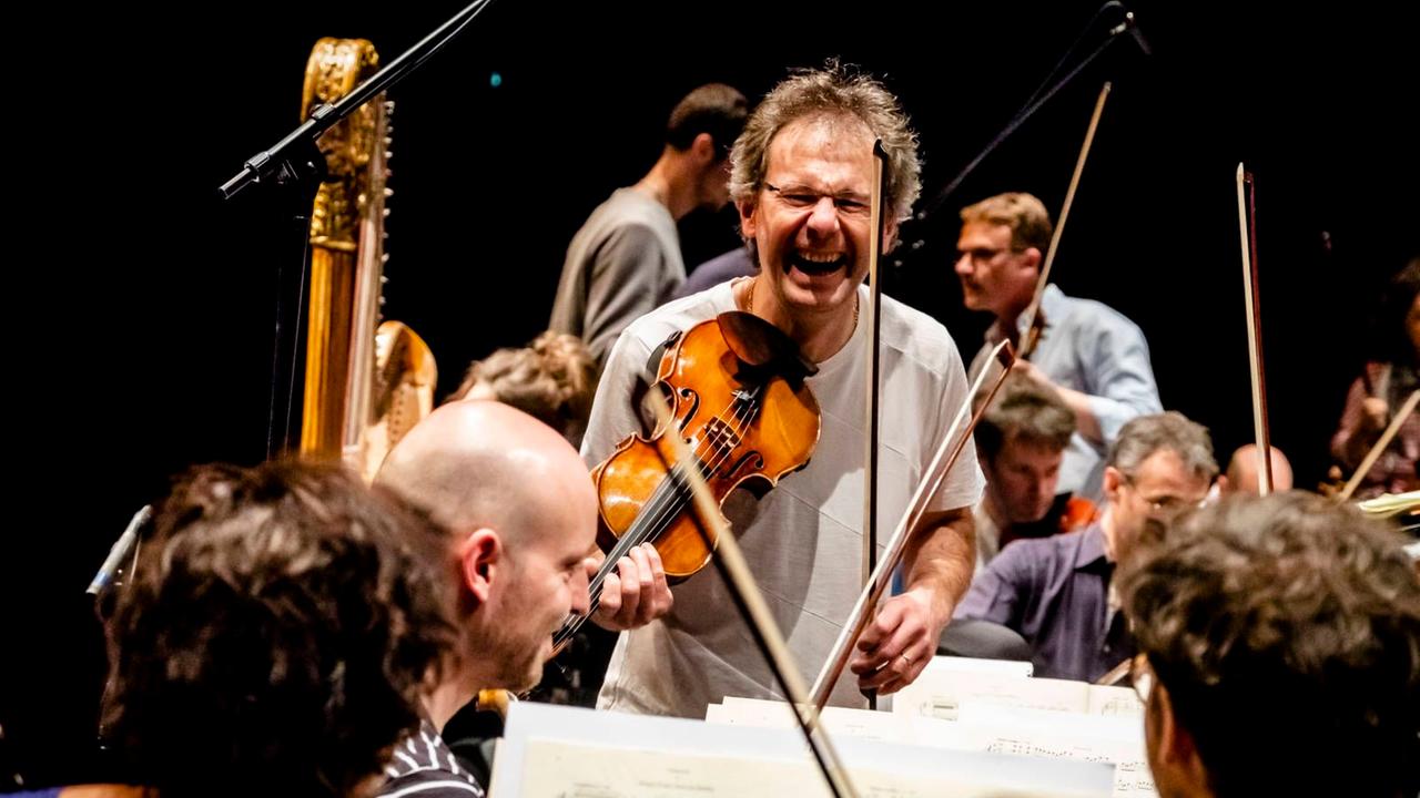 Martial Gauthier hält seine Geige als Linkshänder an die Schulter und lacht dabei in die Kamera im Kreise seiner Musikerkollegen. Martial Gauthier hält seine Geige als Linkshänder an die Schulter und lacht dabei in die Kamera im Kreise seiner Musikerkollegen.