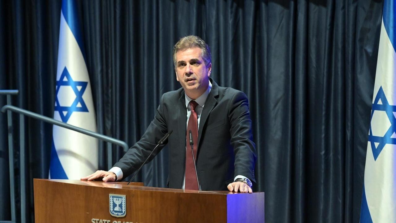Israelischer Außenminister Eli Cohen hält eine Fahne, seitlich sind die Landesflaggen aufgestellt
