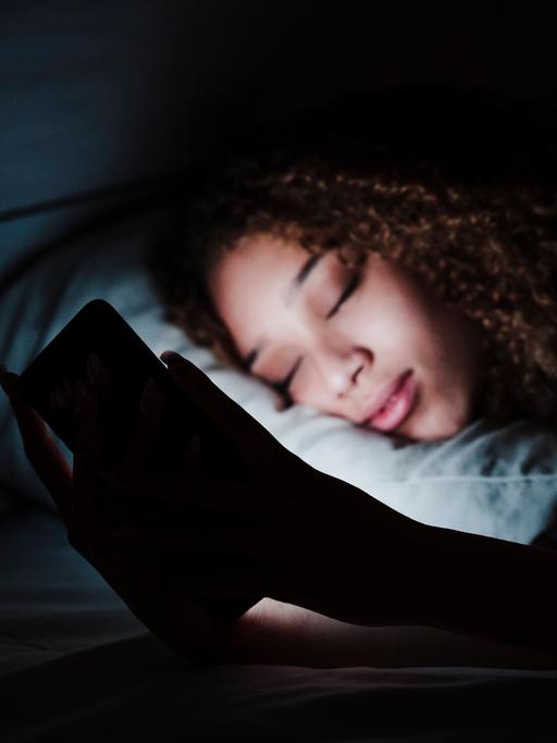 Woman holding mobile phone while sleeping on bed in dark room at home model released Symbolfoto property released EBBF03