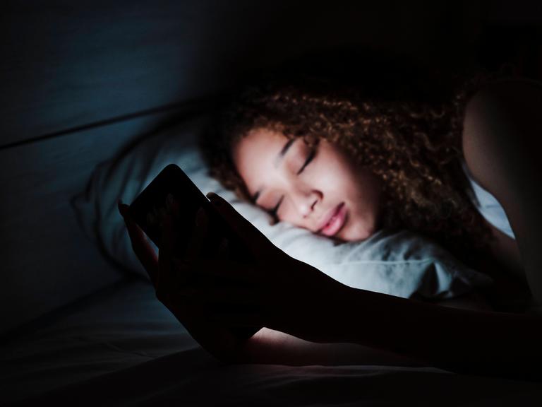 Woman holding mobile phone while sleeping on bed in dark room at home model released Symbolfoto property released EBBF03
